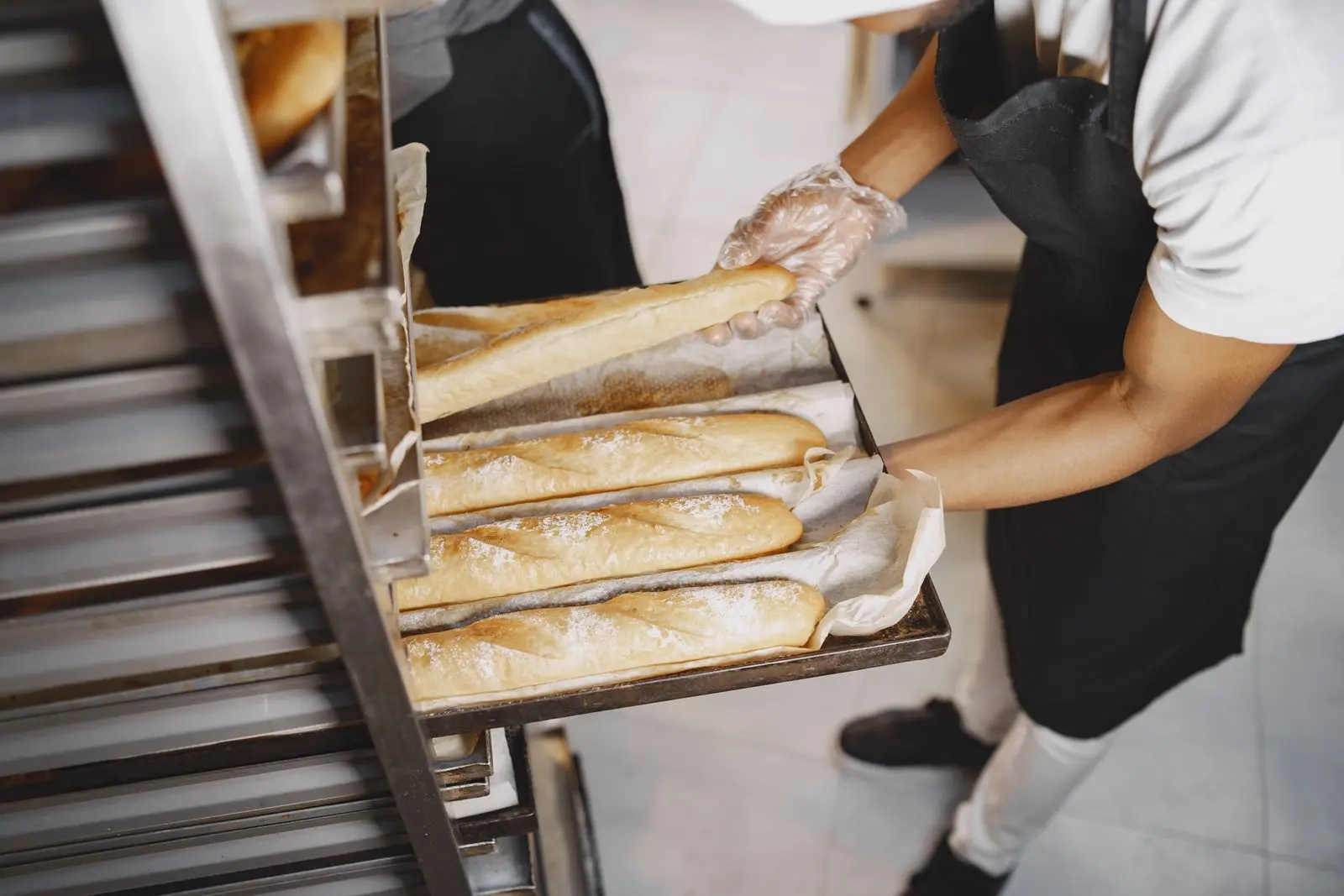 A baker in gloves arranging fresh baguettes on a rack