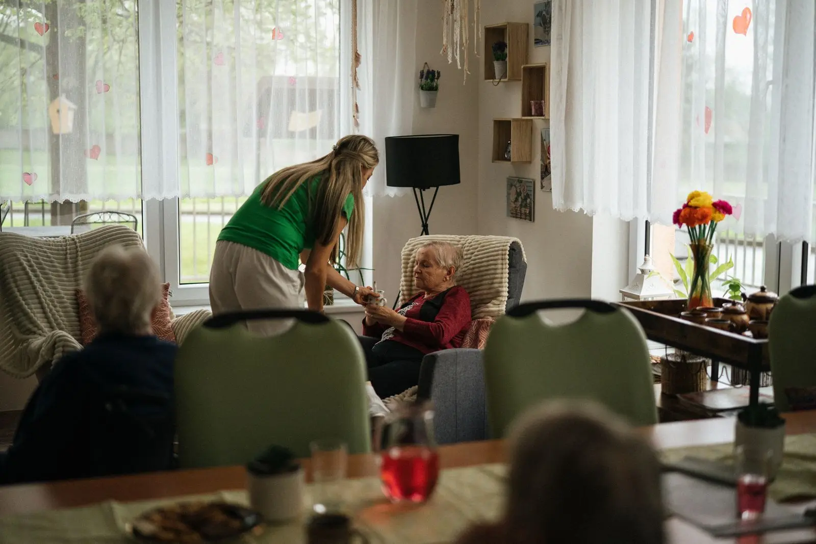 A caregiver serving tea to residents in a bright nursing-home lounge
