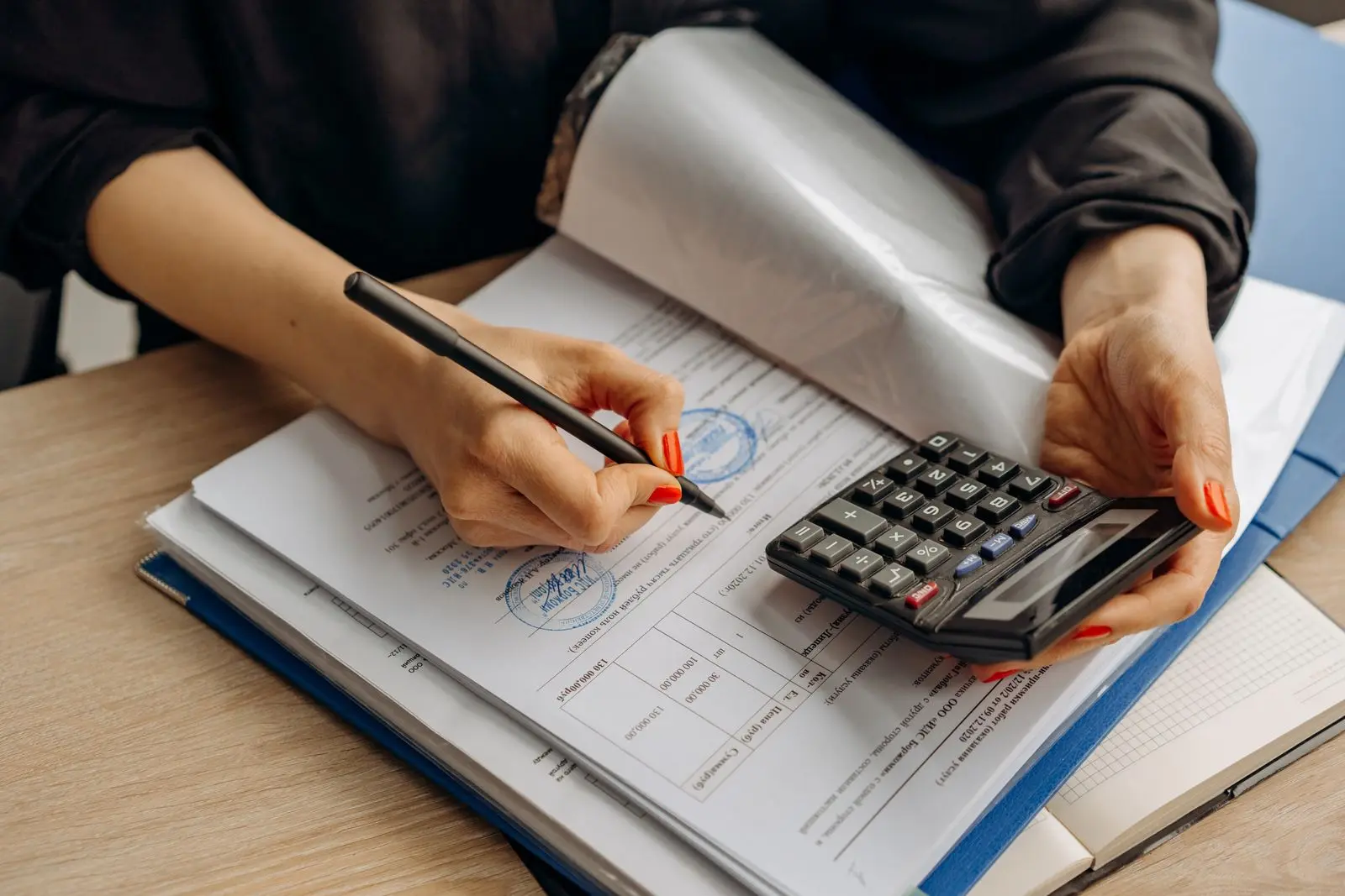 Hands working through invoices with a calculator at an office desk