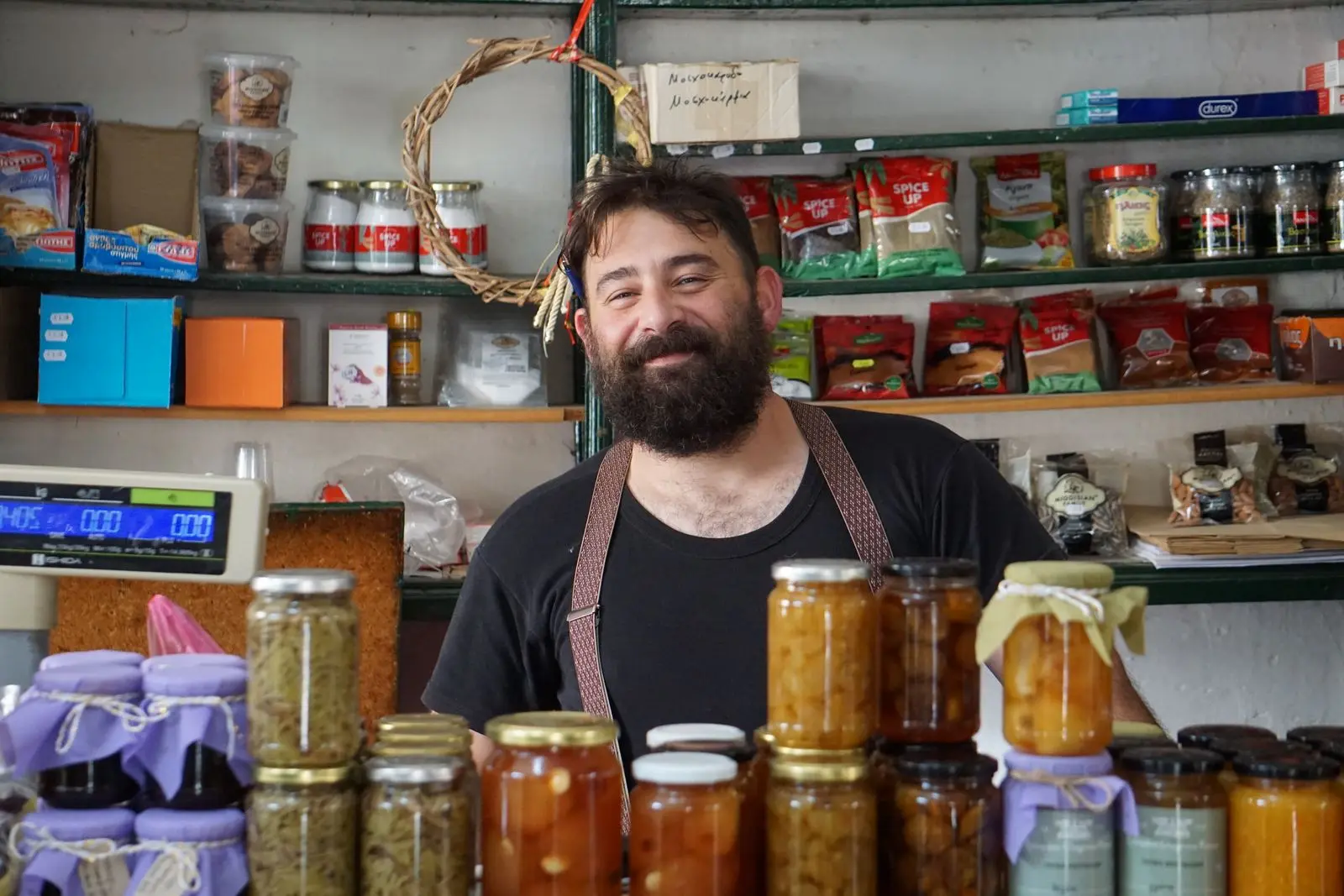 A smiling shopkeeper behind shelves of homemade preserves